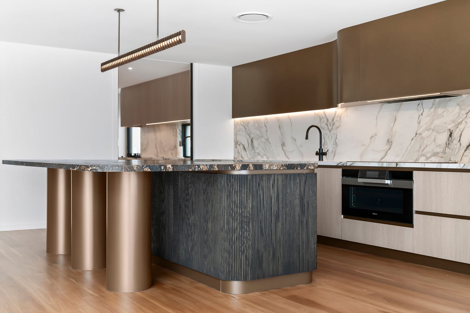 Modern kitchen with marble island and cabinets, wood flooring. Gold and brown tones dominate — PK4 Projects in Port Macquarie, NSW