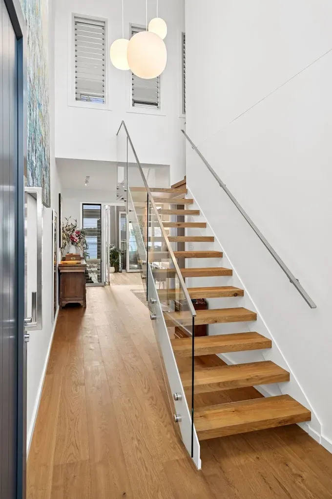 Hallway with wooden floor and staircase with glass railing. White walls, pendant lights — PK4 Projects in Port Macquarie, NSW 