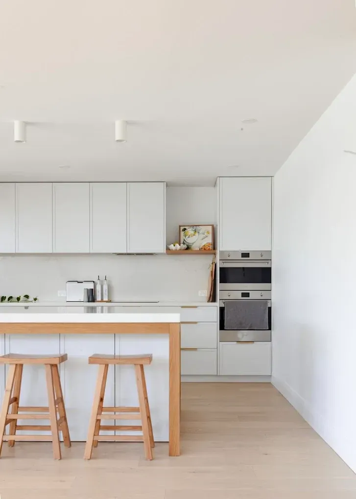 Modern white kitchen with wooden island, stools, cabinetry, and light wood flooring — PK4 Projects in Port Macquarie, NSW 