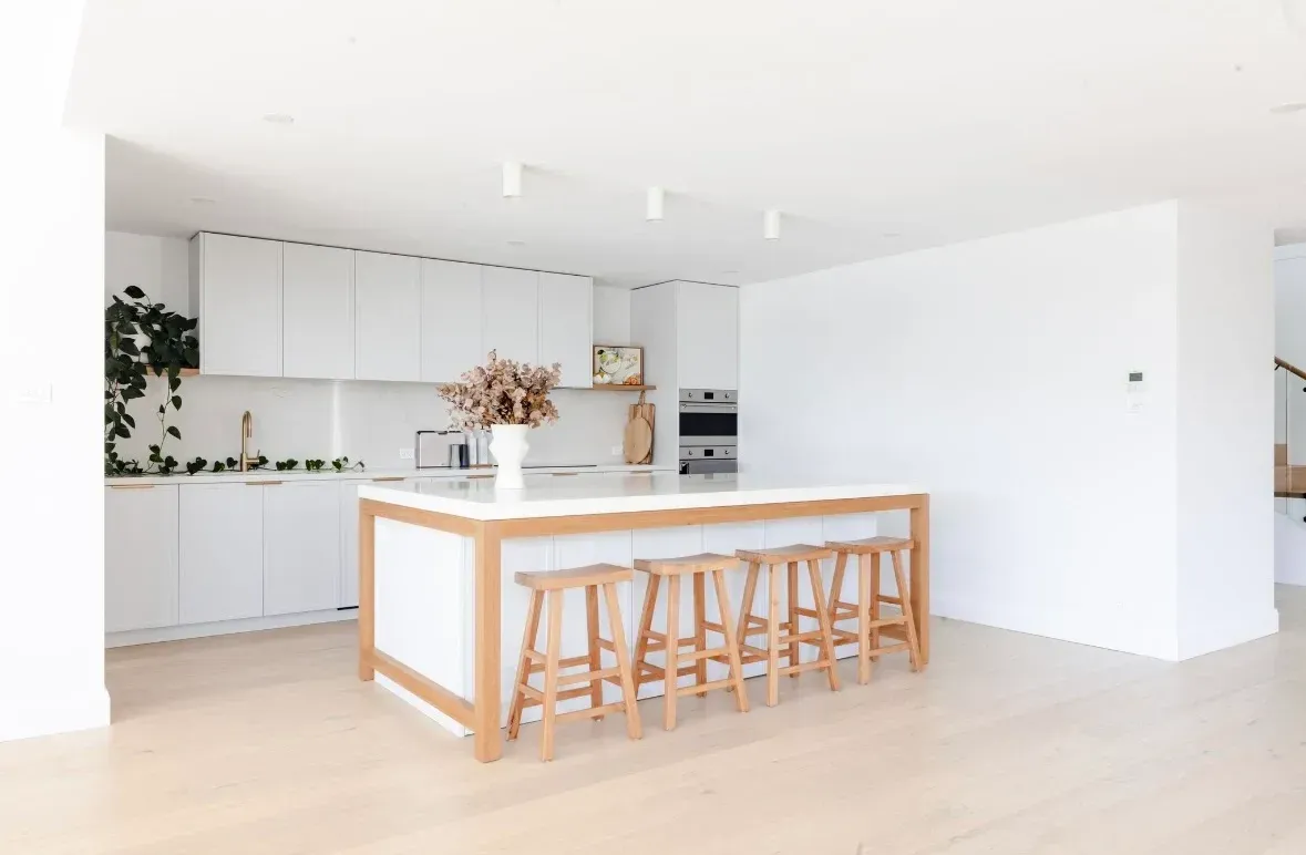 White kitchen with island, wooden stools, cabinets, built-in oven, and dried flowers  — PK4 Projects in Port Macquarie, NSW