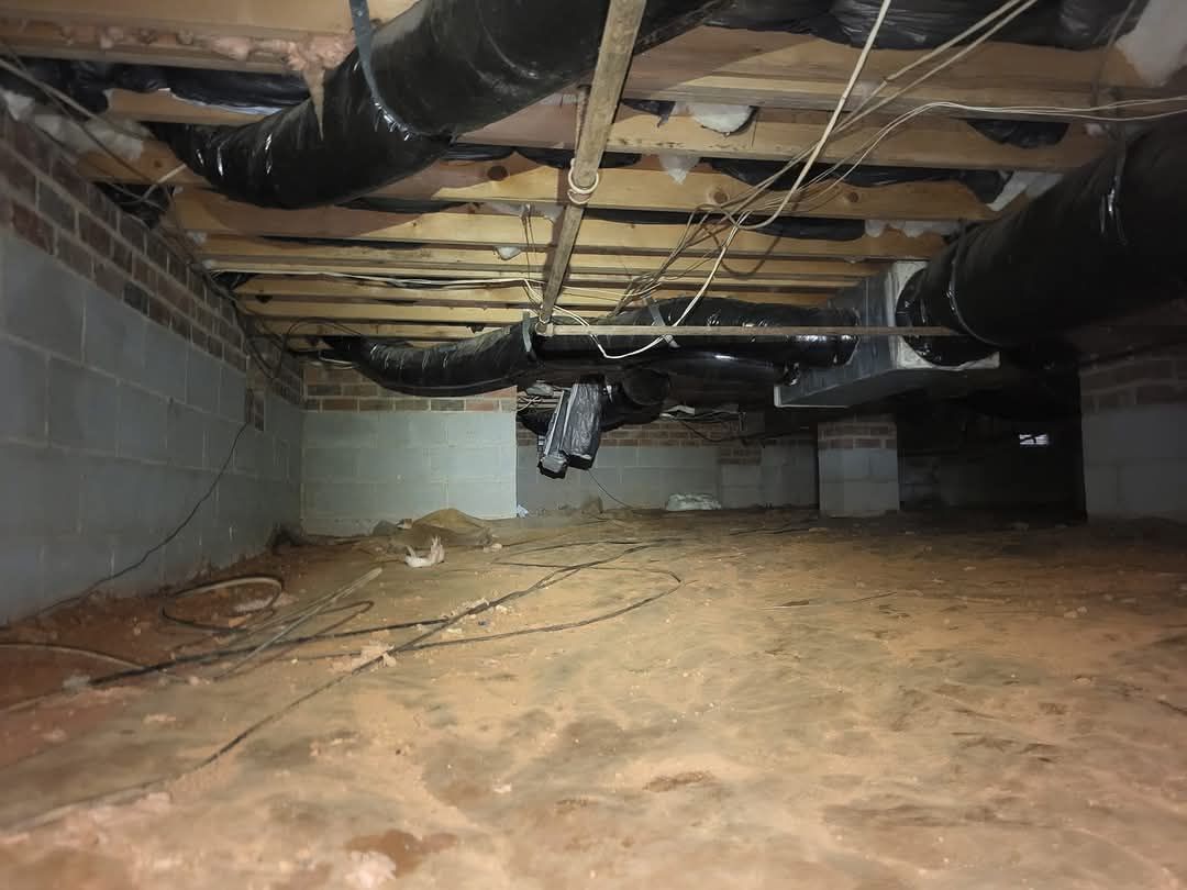 Crawlspace with exposed insulation, ducts, and wooden joists above a dirt floor