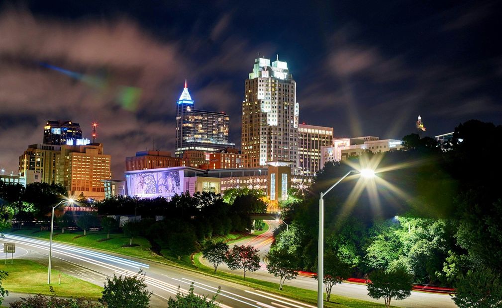 Nighttime city skyline with illuminated buildings, a lit street, and a bright starburst streetlight in the foreground