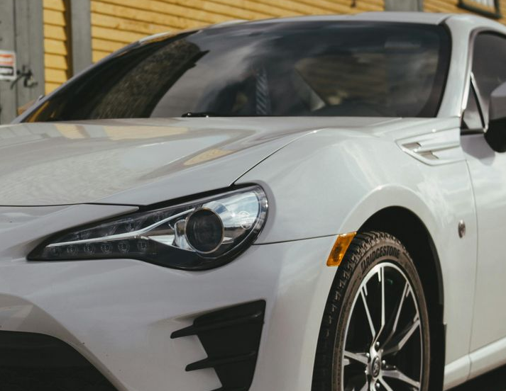 White sports car parked in front of a yellow building, with clear headlight.