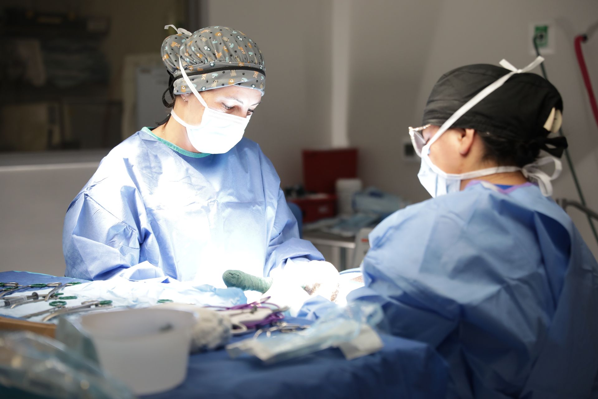 Two surgeons in blue scrubs operating under bright surgical lights in an operating room