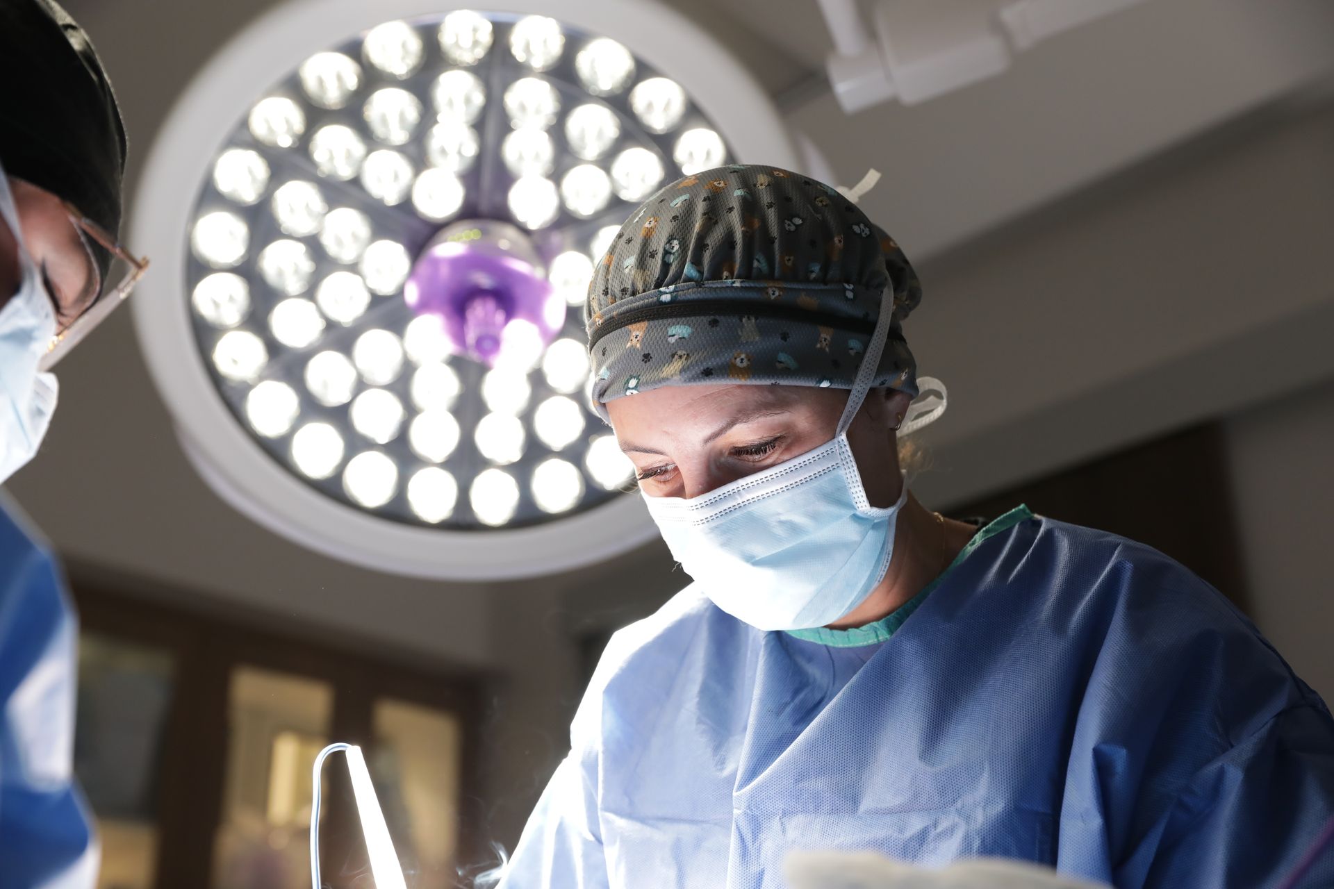 Surgeons in blue scrubs and masks under bright operating room lights during a procedure