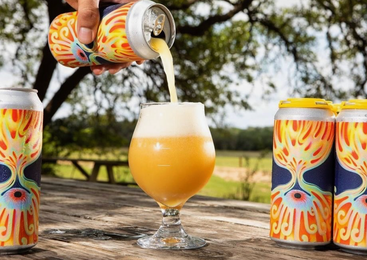 Beer being poured into a glass on a picnic table, with colorful cans outdoors