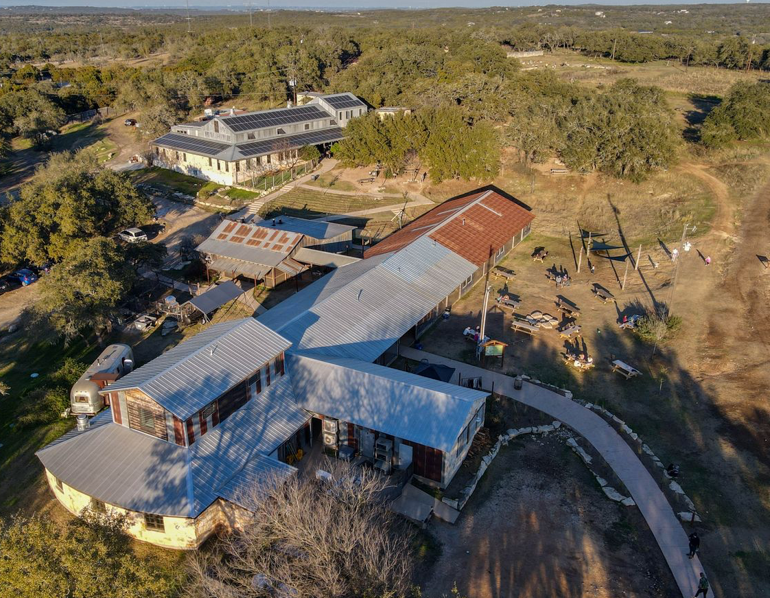 Aerial view of a rural property with metal-roofed buildings, dirt roads, and surrounding trees
