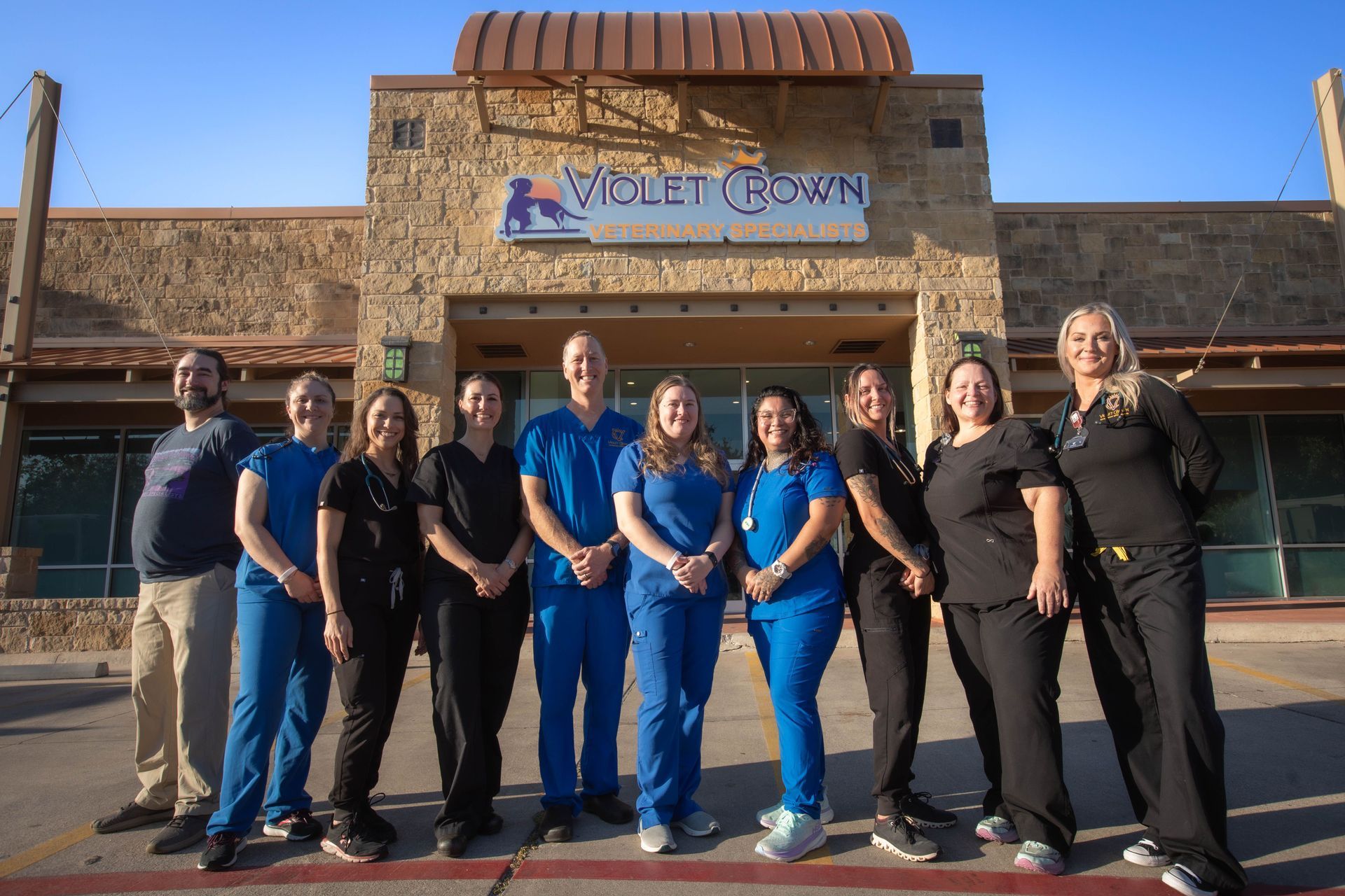 Group of employees standing outside a storefront entrance in dark uniforms, posing for a photo.