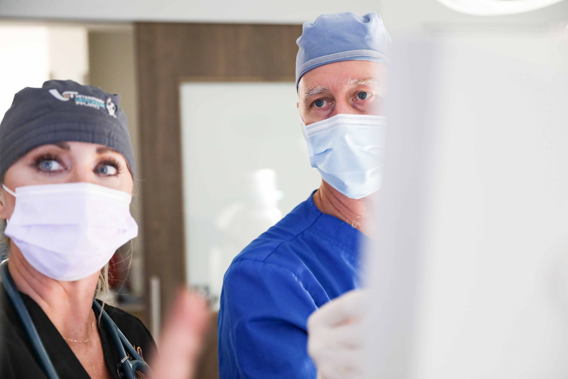 Masked medical staff in blue scrubs looking at a monitor in a hospital setting