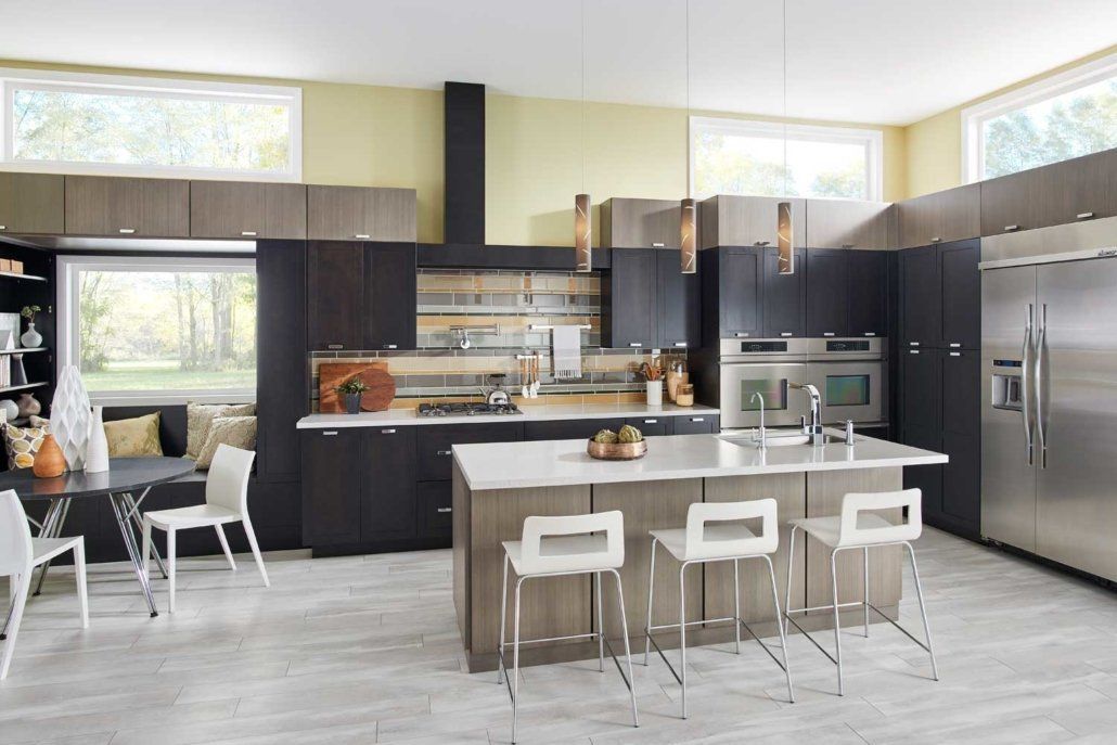 Modern kitchen with large island, white stools, dark cabinets, stainless steel appliances, and bright windows
