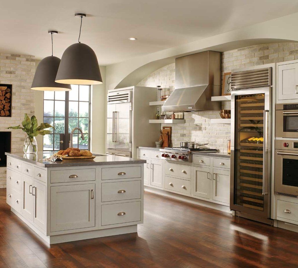 Modern white kitchen with island, pendant lights, hardwood floors, and stainless steel appliances