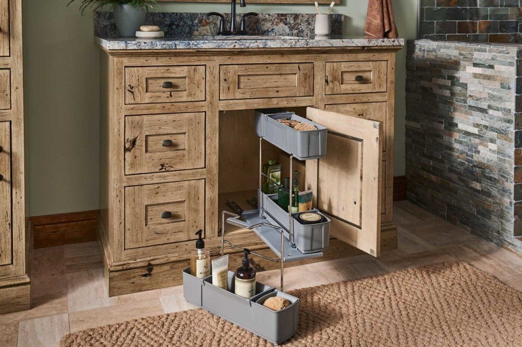 Wooden kitchen cabinet with pull-out drawer organizers open on a beige rug in a rustic kitchen