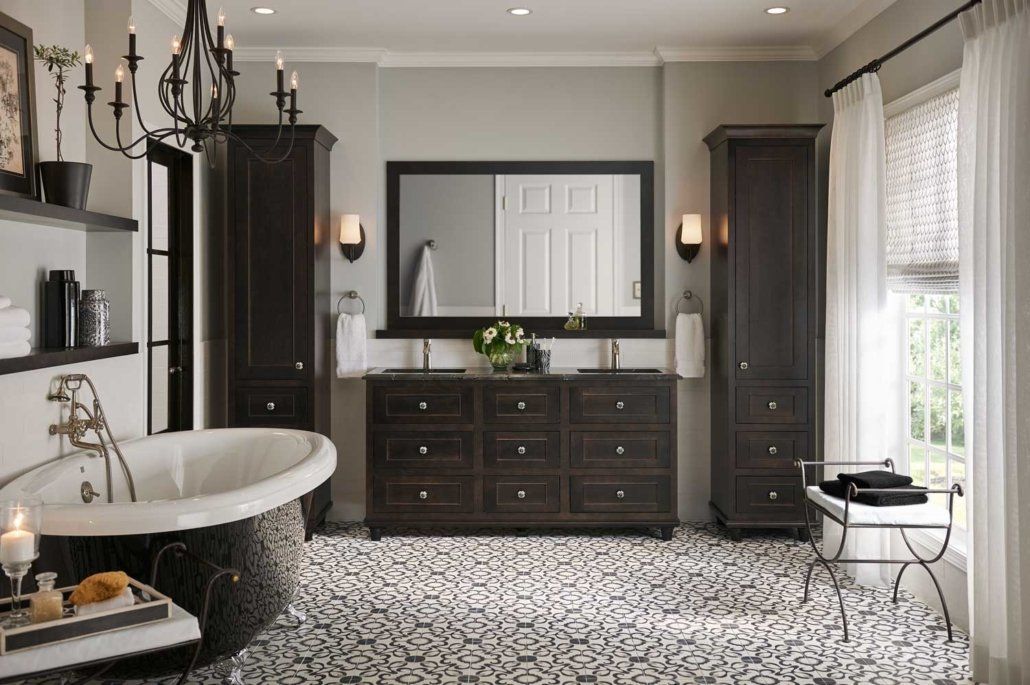 Elegant black-and-white bathroom with pedestal tub, vanity, mirror, and patterned floor tiles.