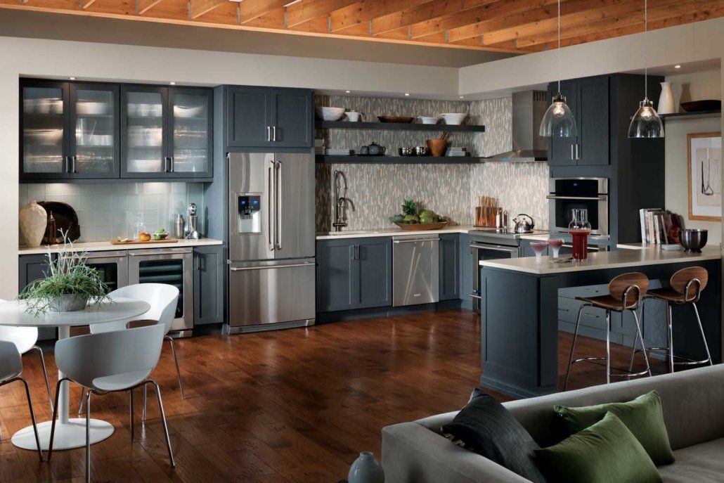 Modern open-plan kitchen and living room with dark cabinets, stainless steel appliances, wood floors, and green accents