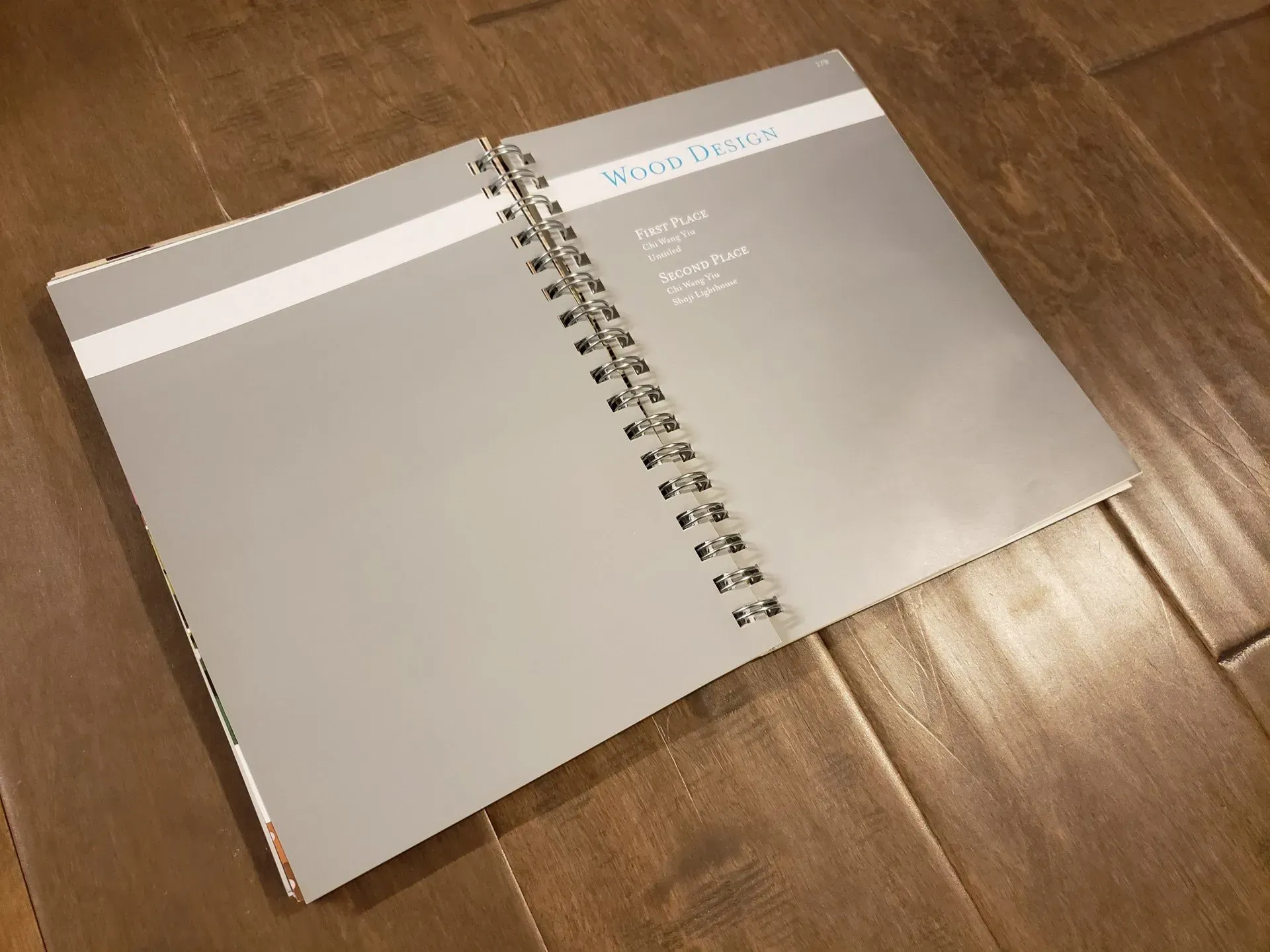 Open spiral notebook with blank beige pages on a wooden floor.
