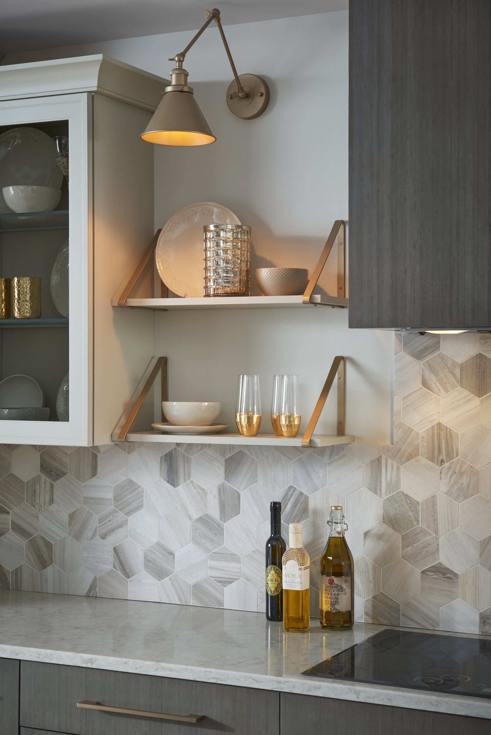 Modern kitchen corner with open shelves, hanging lamp, patterned backsplash, and bottles on a marble countertop