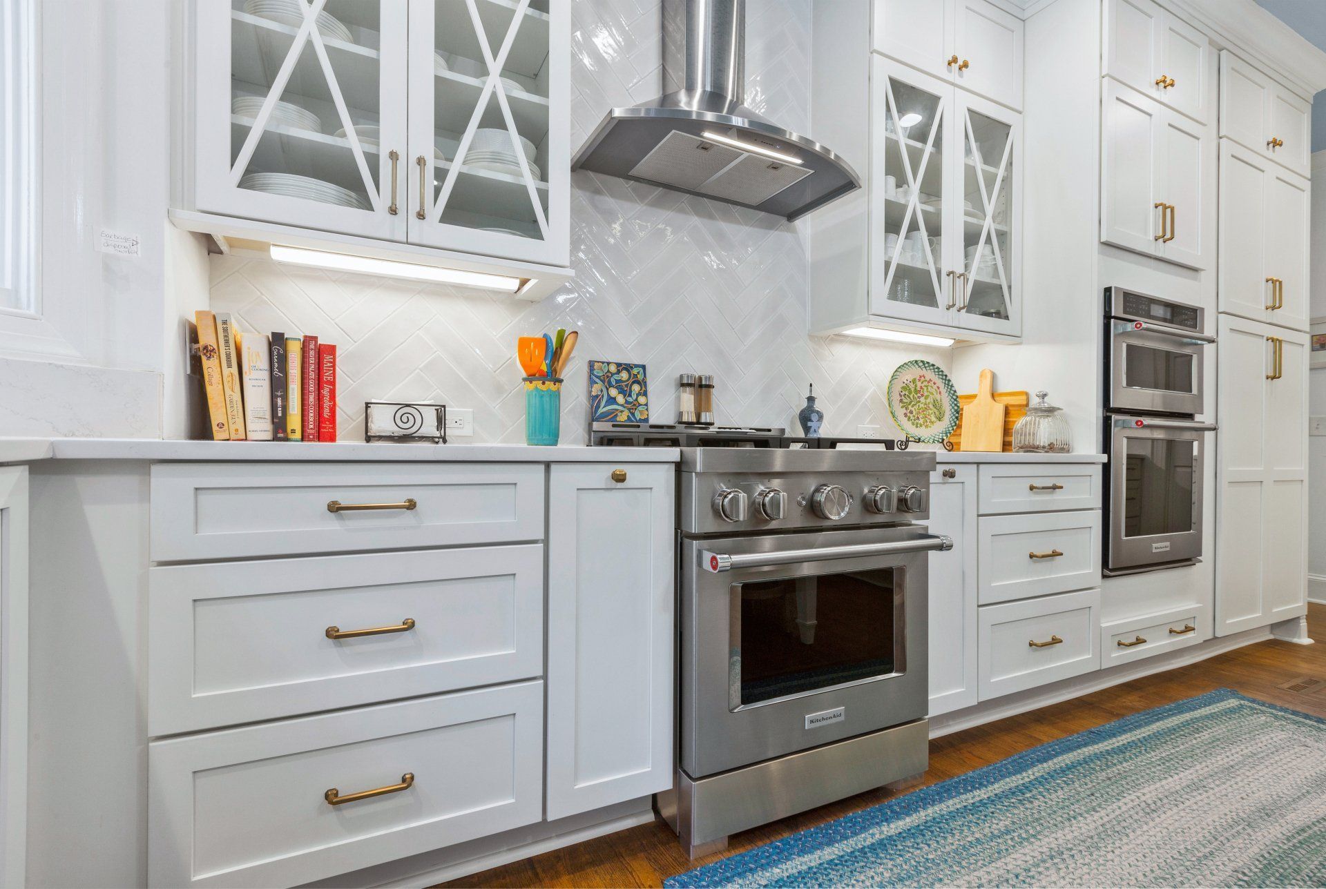 Bright white modern kitchen with glass cabinets, stainless steel stove, and turquoise rug