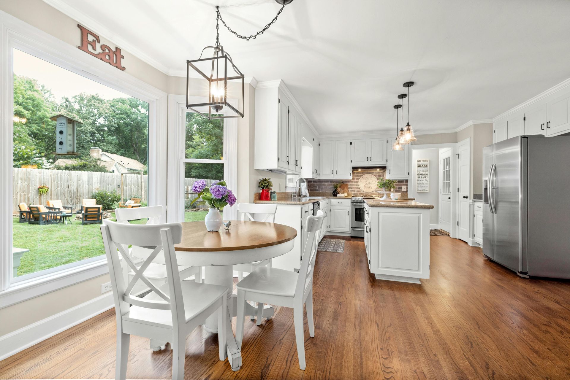 Bright white kitchen and dining area with wooden floors, round table, and large window overlooking a garden