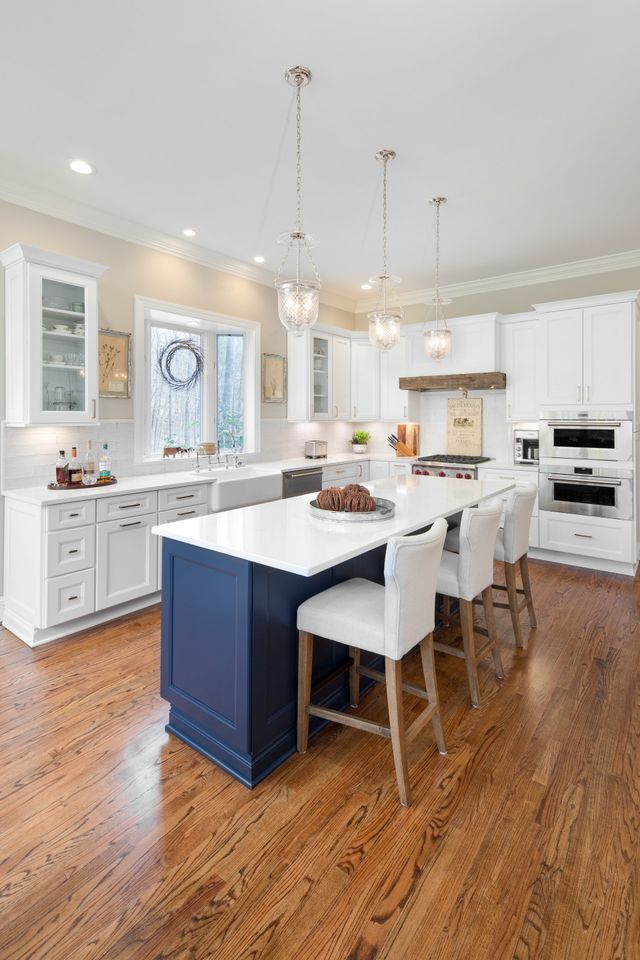 Bright white kitchen with an island, bar stools, and hardwood floors, lit by pendant lights.