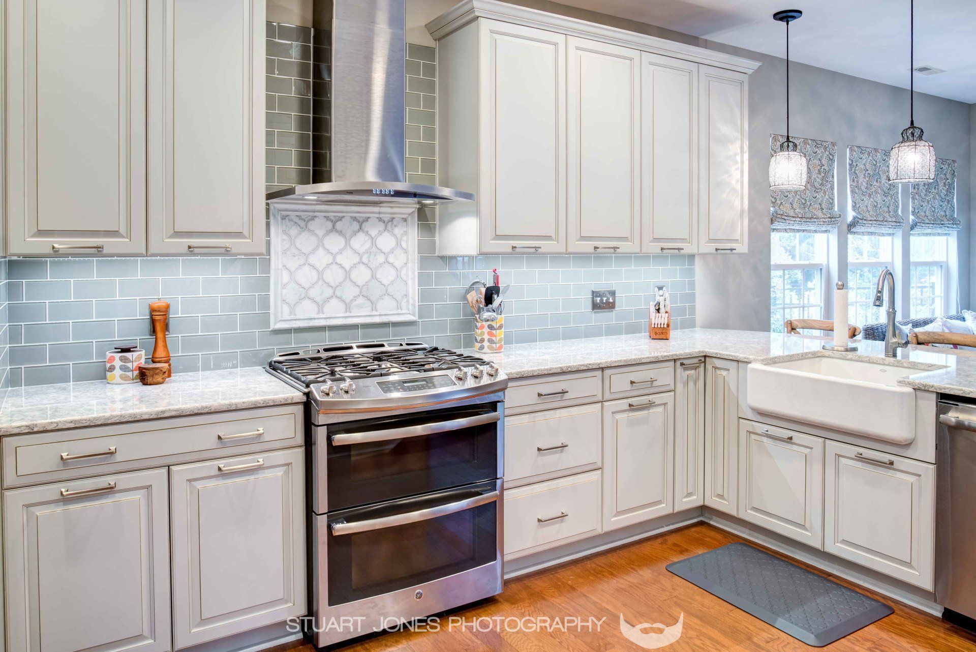 Bright modern kitchen with white cabinets, gray tile backsplash, stainless steel stove, and island sink