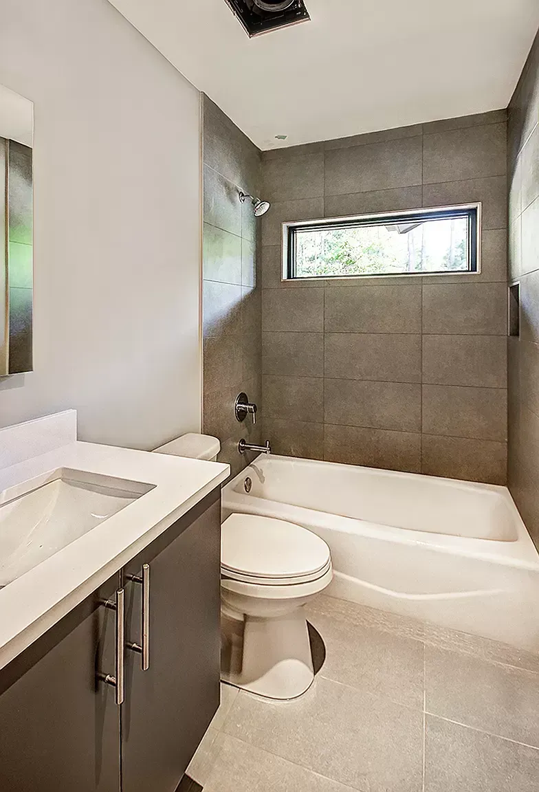 Modern bathroom with white tub, gray tile shower, and vanity sink.