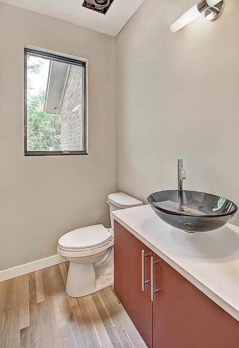 Small bathroom with toilet, black vessel sink vanity, white walls, and a window.