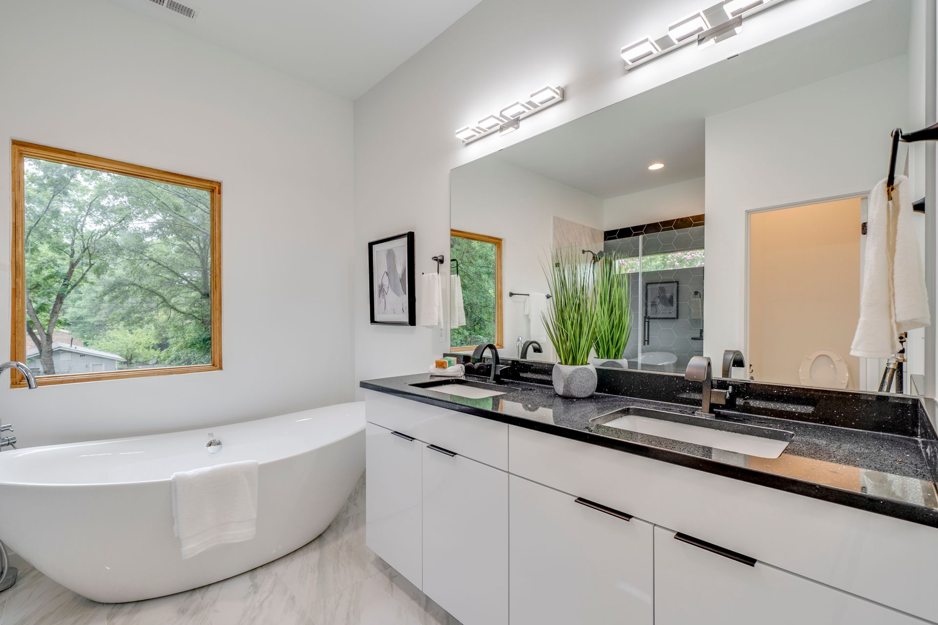 Bright modern bathroom with a freestanding tub, double vanity, and large mirror-lit countertop.