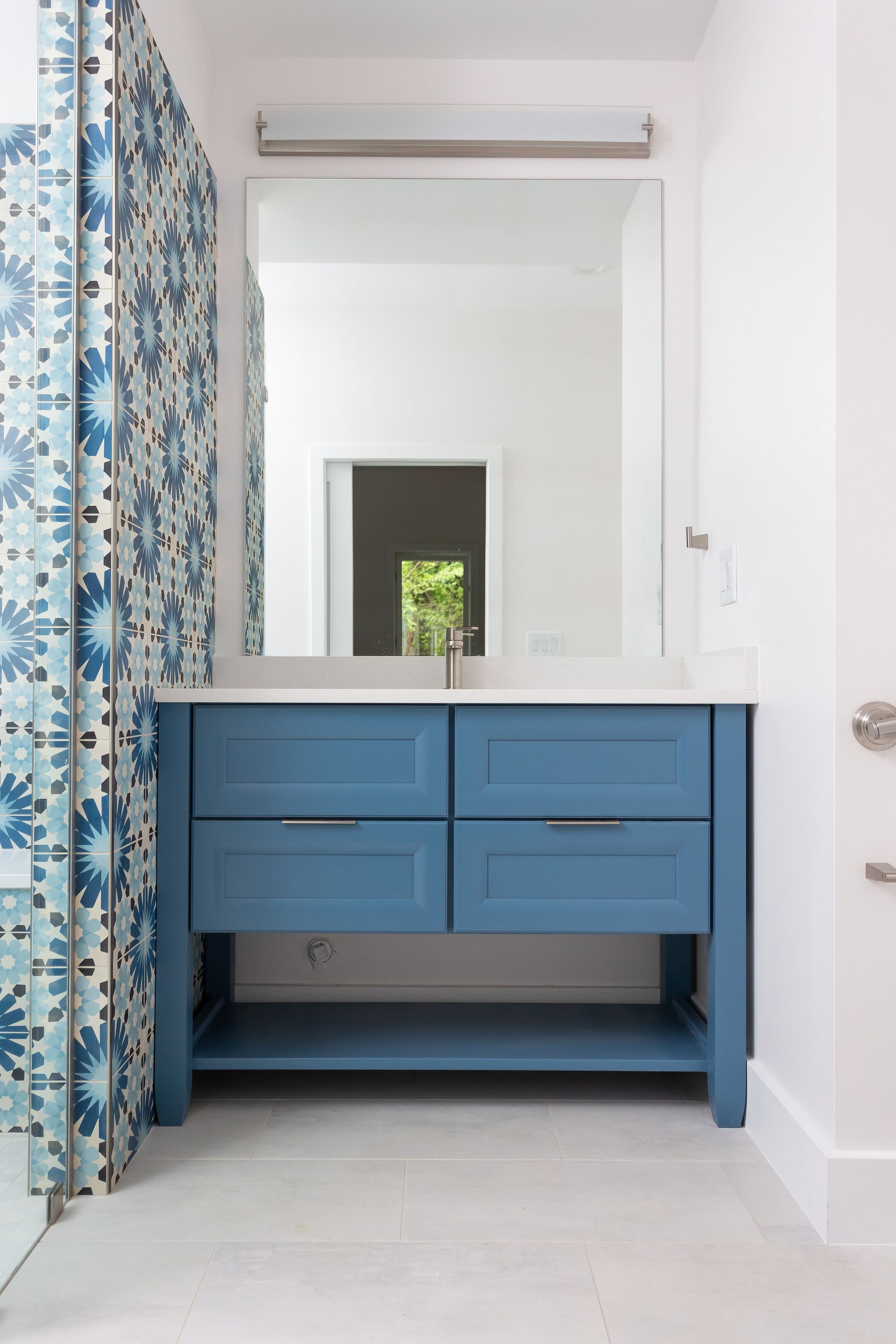 Blue vanity with mirror in a bright bathroom, beside a floral curtain and white door