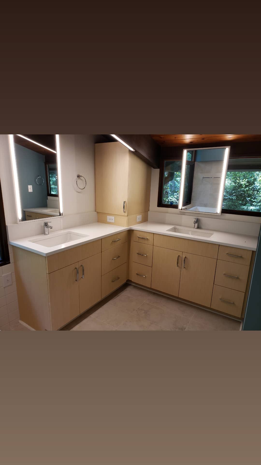 Spacious beige kitchen with white countertops, wood cabinets, and a window overlooking greenery.