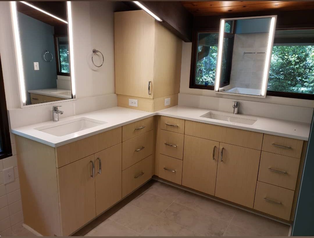 Corner bathroom vanity with two sinks, beige cabinets, mirrors, and windows above counter tops.