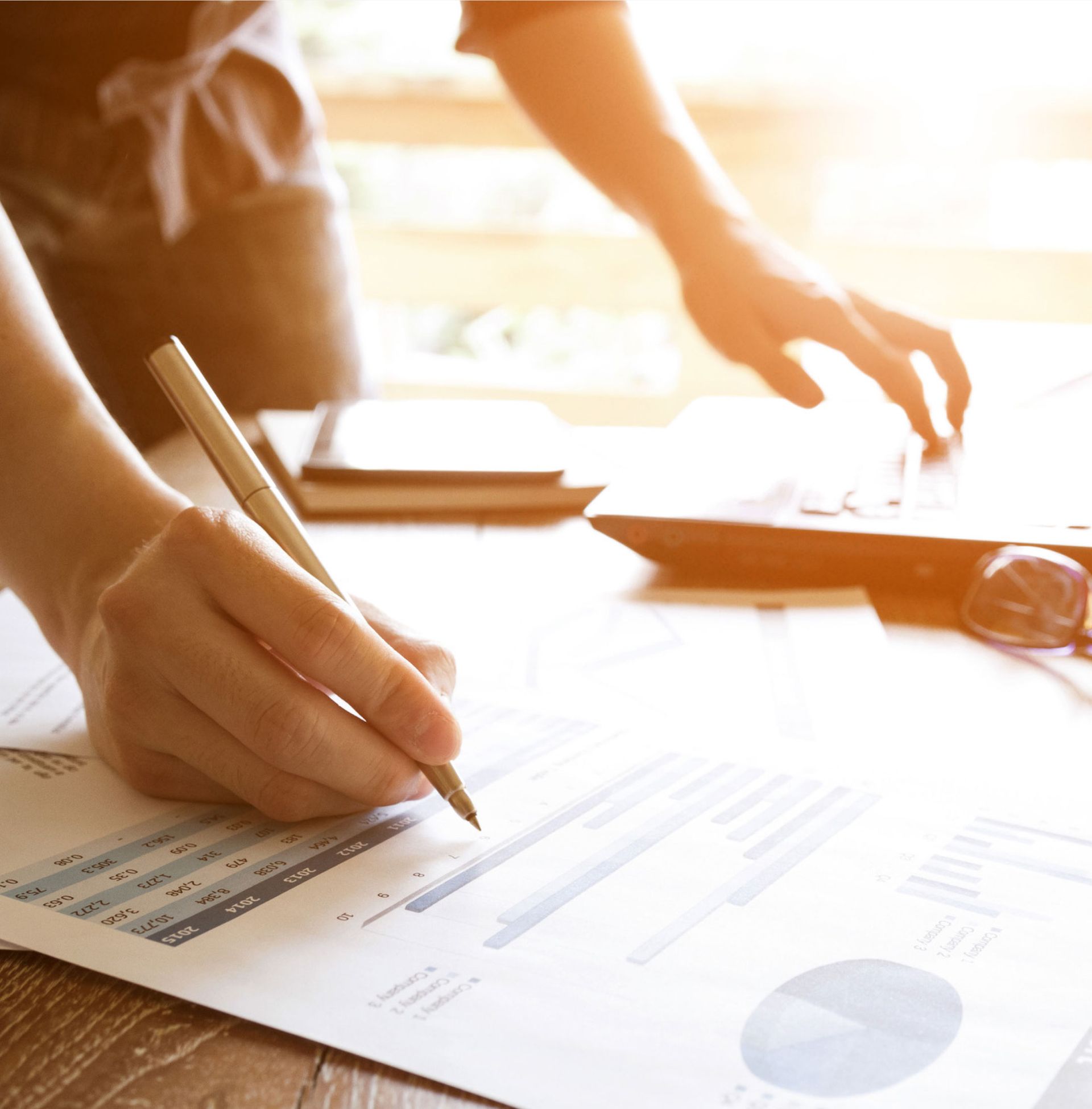 Hands reviewing financial documents with a pen at a sunlit desk
