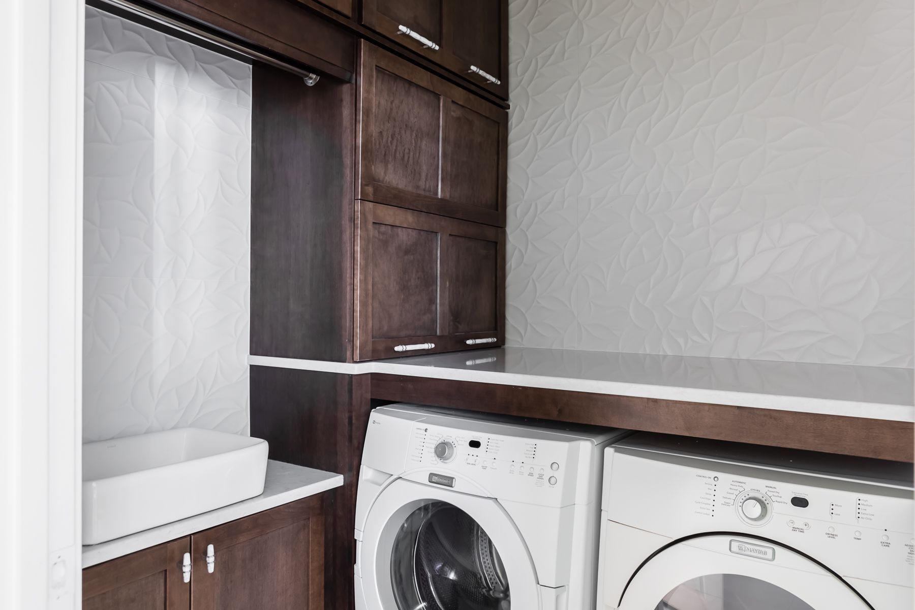 Laundry room with stacked washer and dryer beside dark wood cabinets and a countertop.