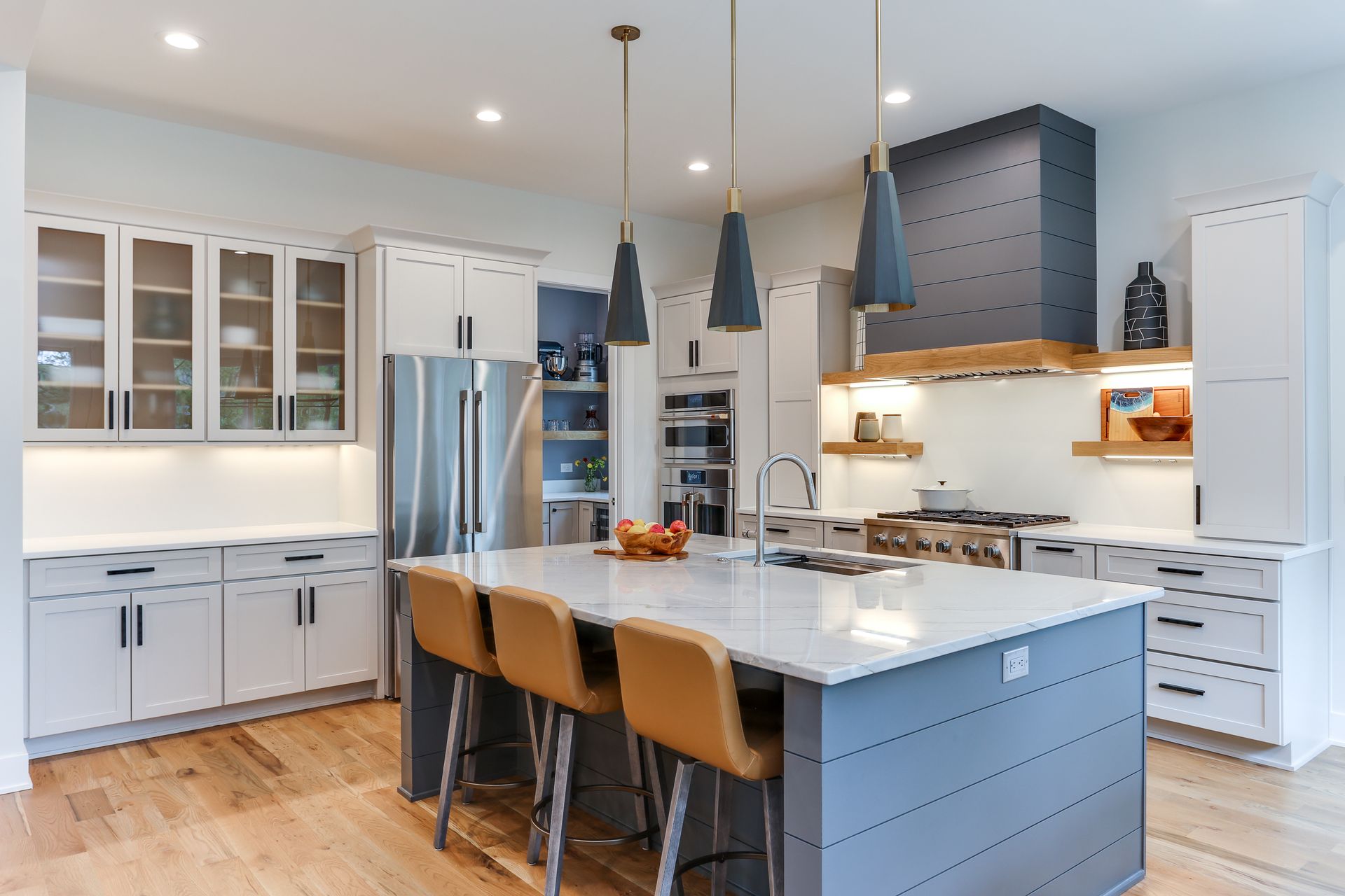 Modern kitchen with white cabinets, blue island, pendant lights, and stainless steel appliances