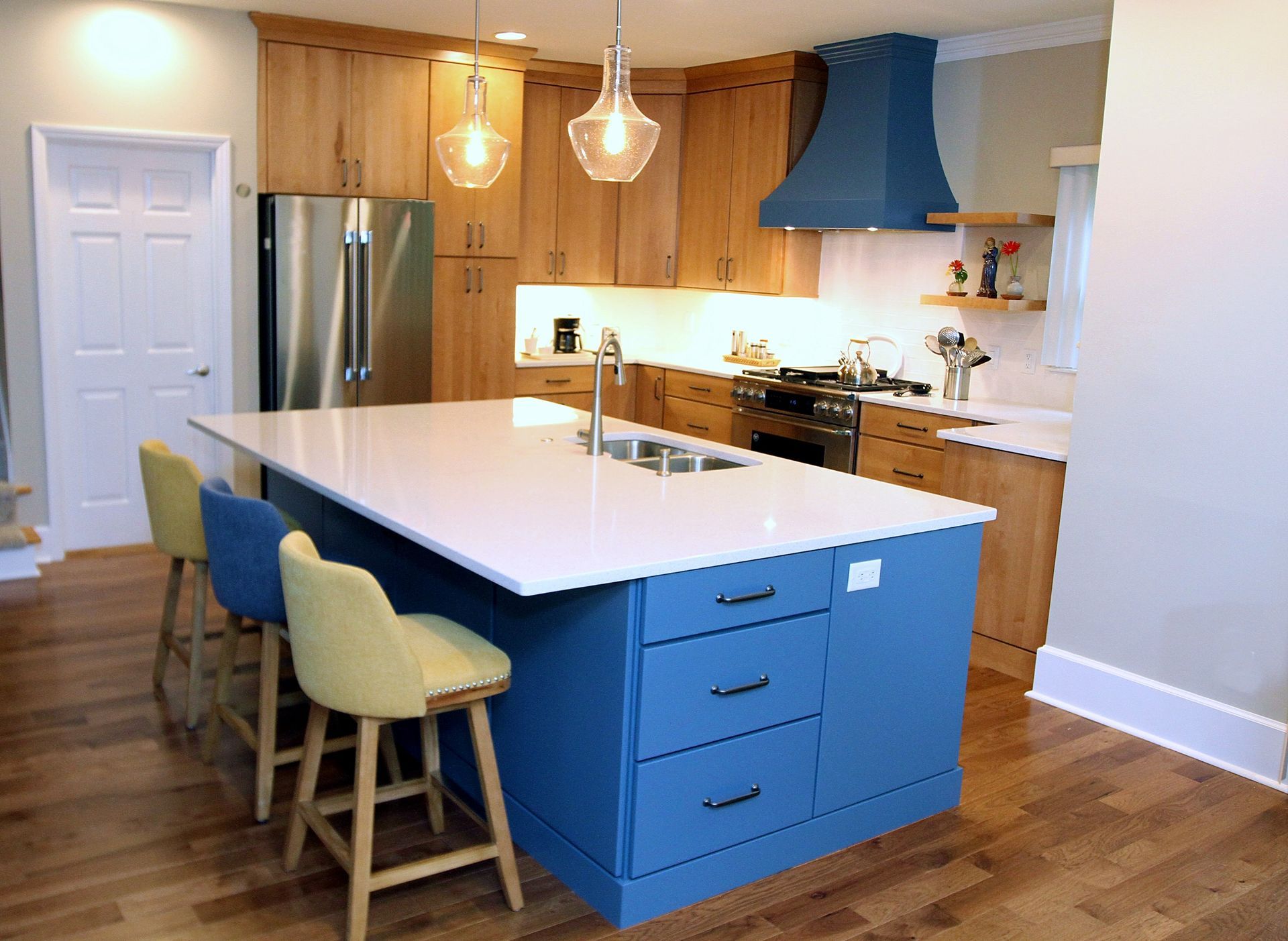 Bright kitchen with blue island, wood cabinets, stainless fridge, and two stools