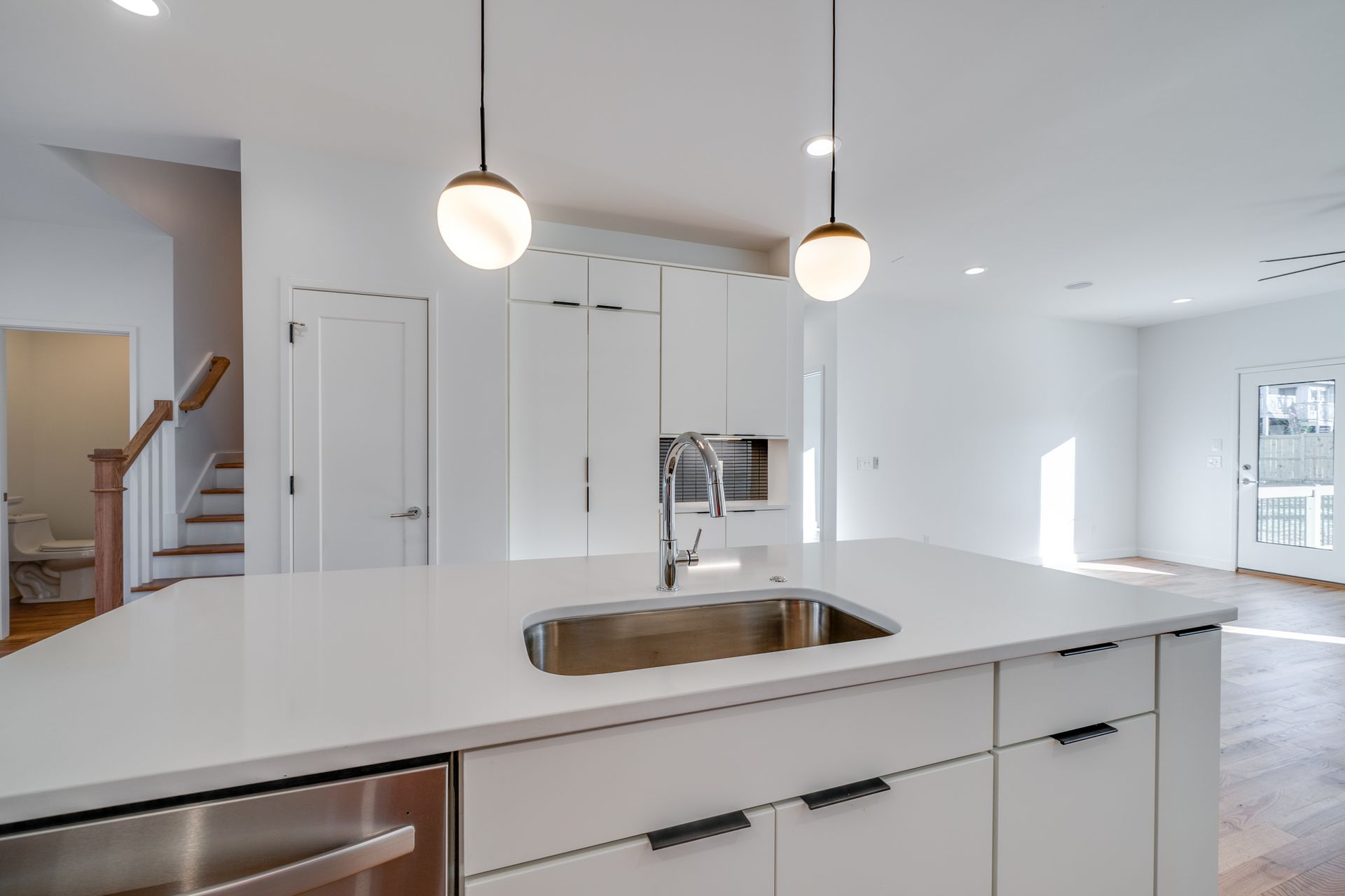 Modern white kitchen with island, pendant lights, and stainless steel sink in an open floor plan
