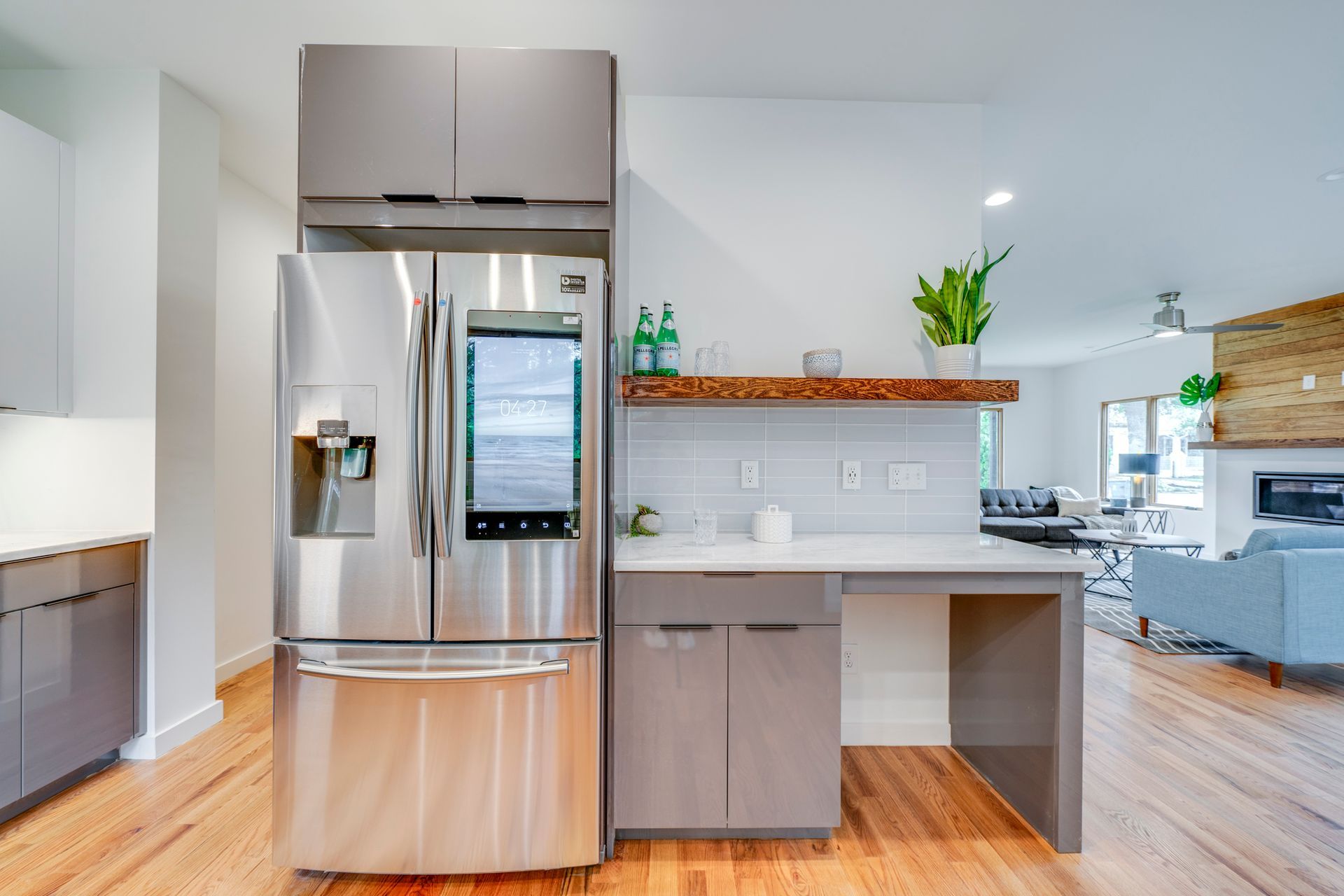Modern kitchen with stainless steel refrigerator, wood cabinets, white backsplash, and open living area