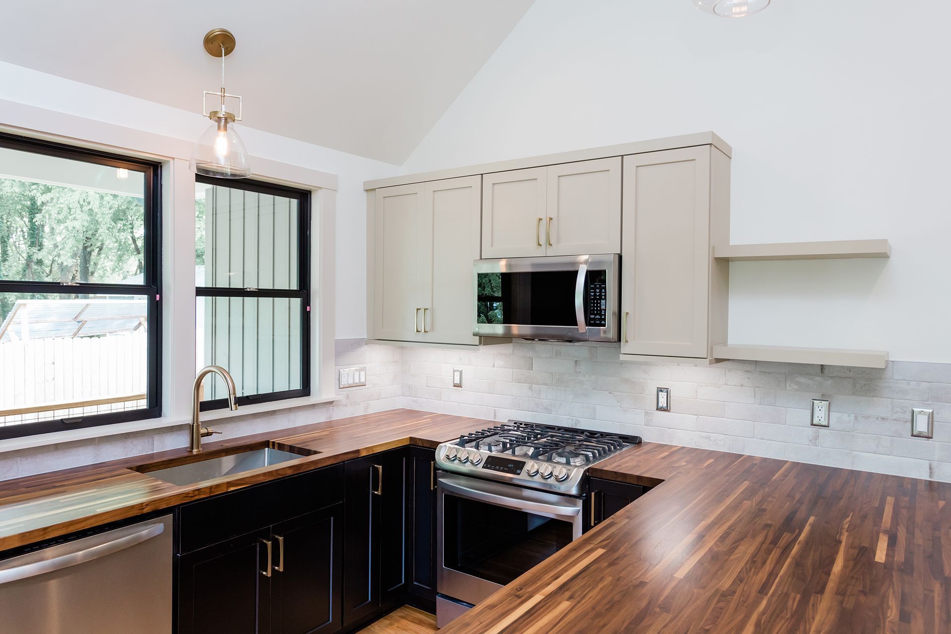 Bright modern kitchen with white cabinets, black lower cabinets, wood countertops, and a large window