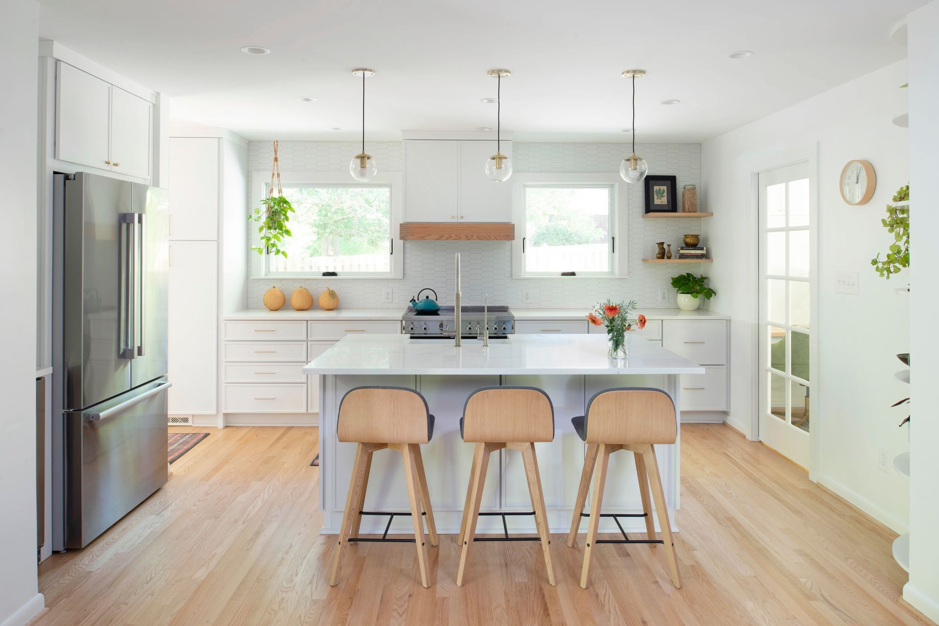 Bright modern kitchen with white cabinets, stainless fridge, island seating, and wood floors