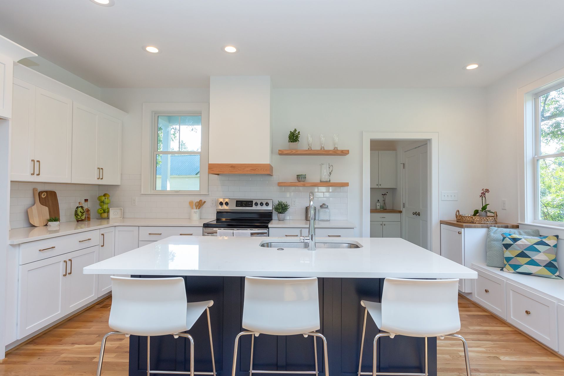 Bright white kitchen with a large island, wood floors, and sunlit windows