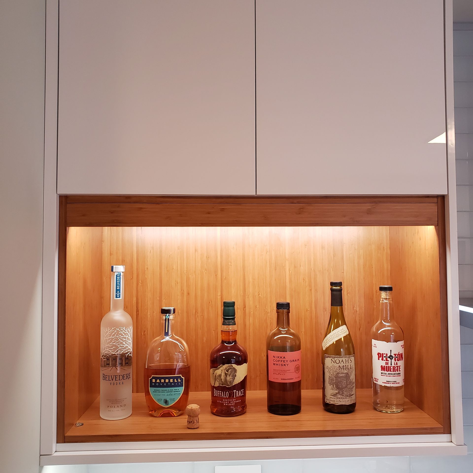 Lit display shelf with six liquor bottles on a wooden backlit cabinet