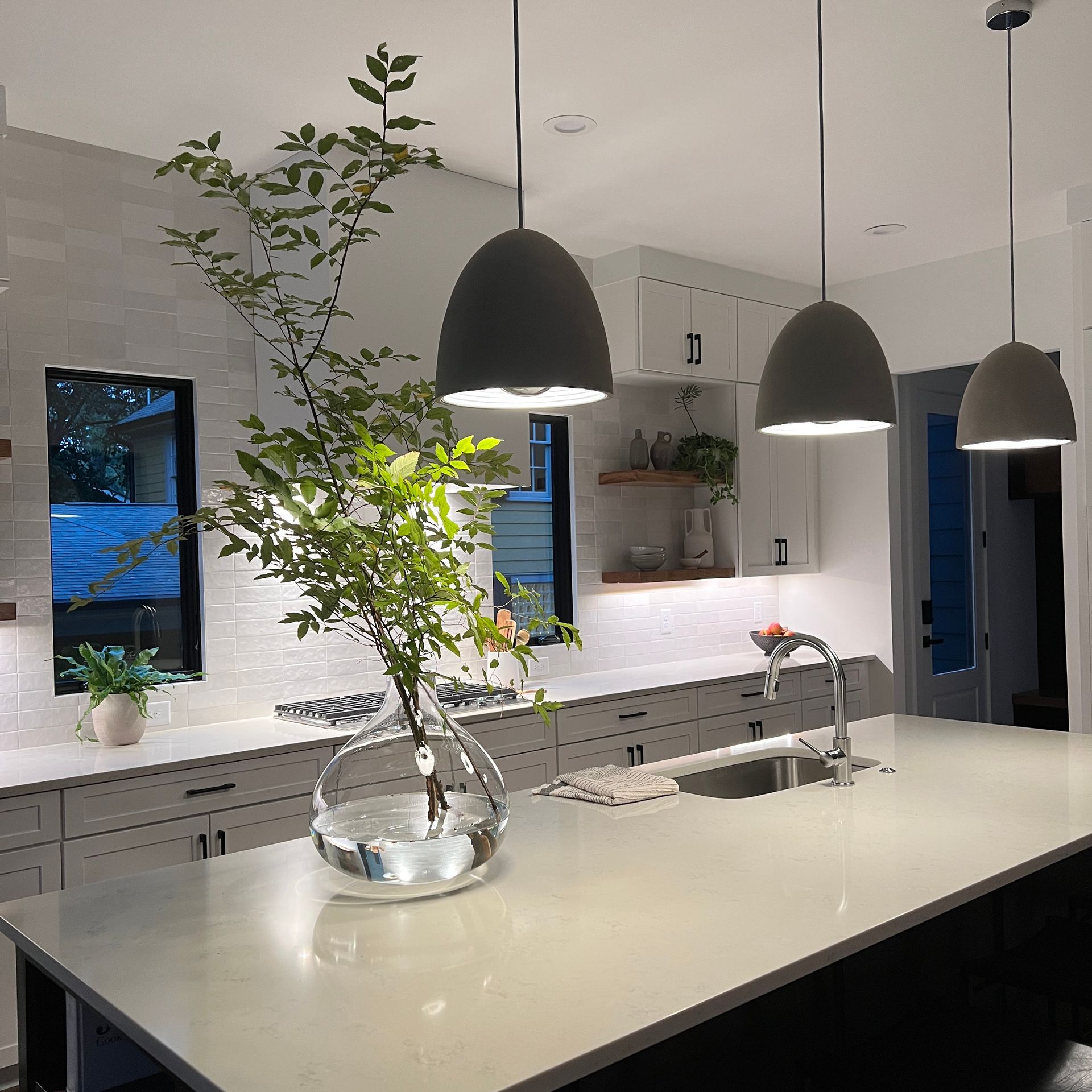 Modern kitchen with white island, pendant lights, stainless sink, and a vase of branches on the counter