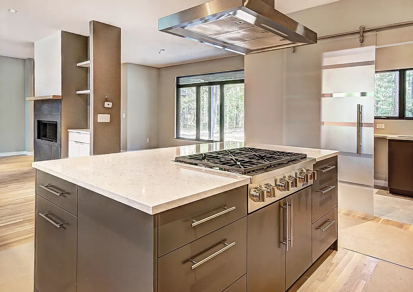 Modern kitchen with island, white countertops, gas range, and large windows with wood flooring