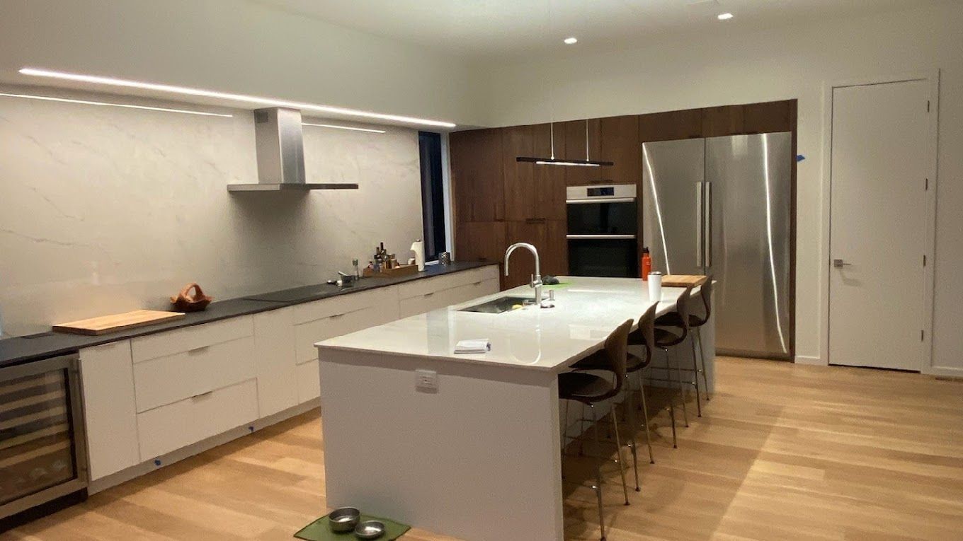 Modern kitchen with white island, wood floors, stainless steel appliances, and pendant lights