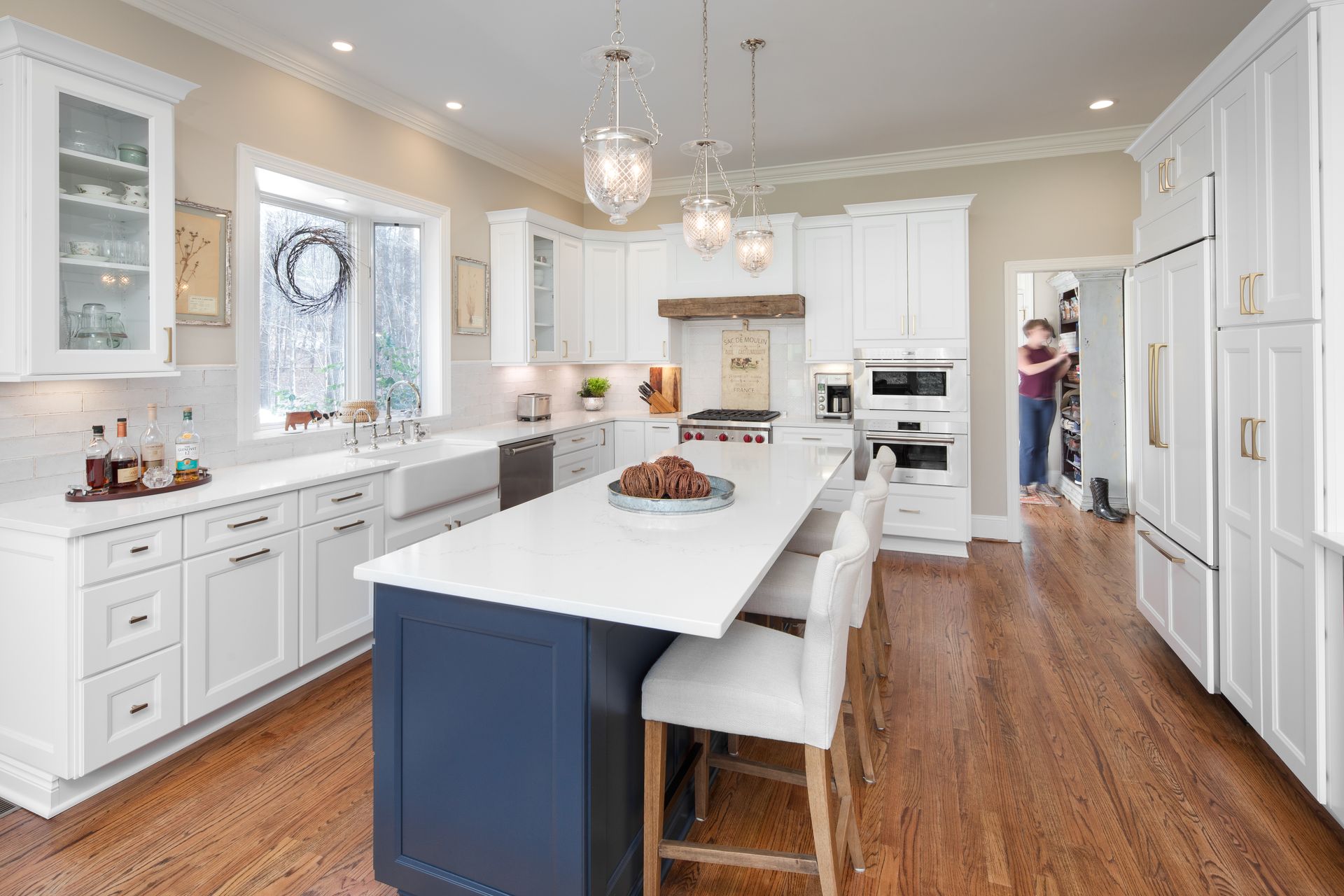 Bright white kitchen with large island, hardwood floors, and a person near the doorway