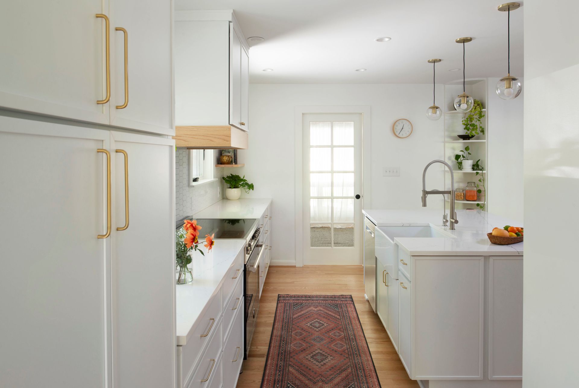 Bright white galley kitchen with gold hardware, red runner, and island under pendant lights
