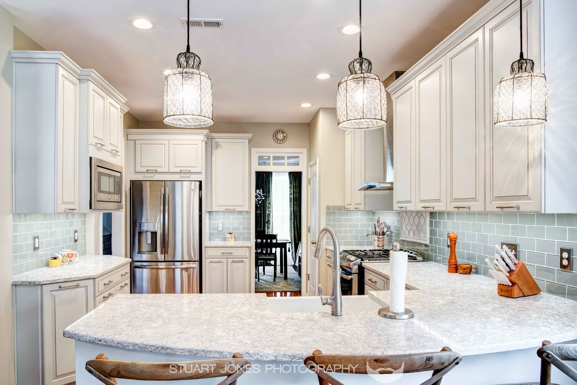 Bright modern kitchen with white cabinets, marble island, stainless fridge, and pendant lights