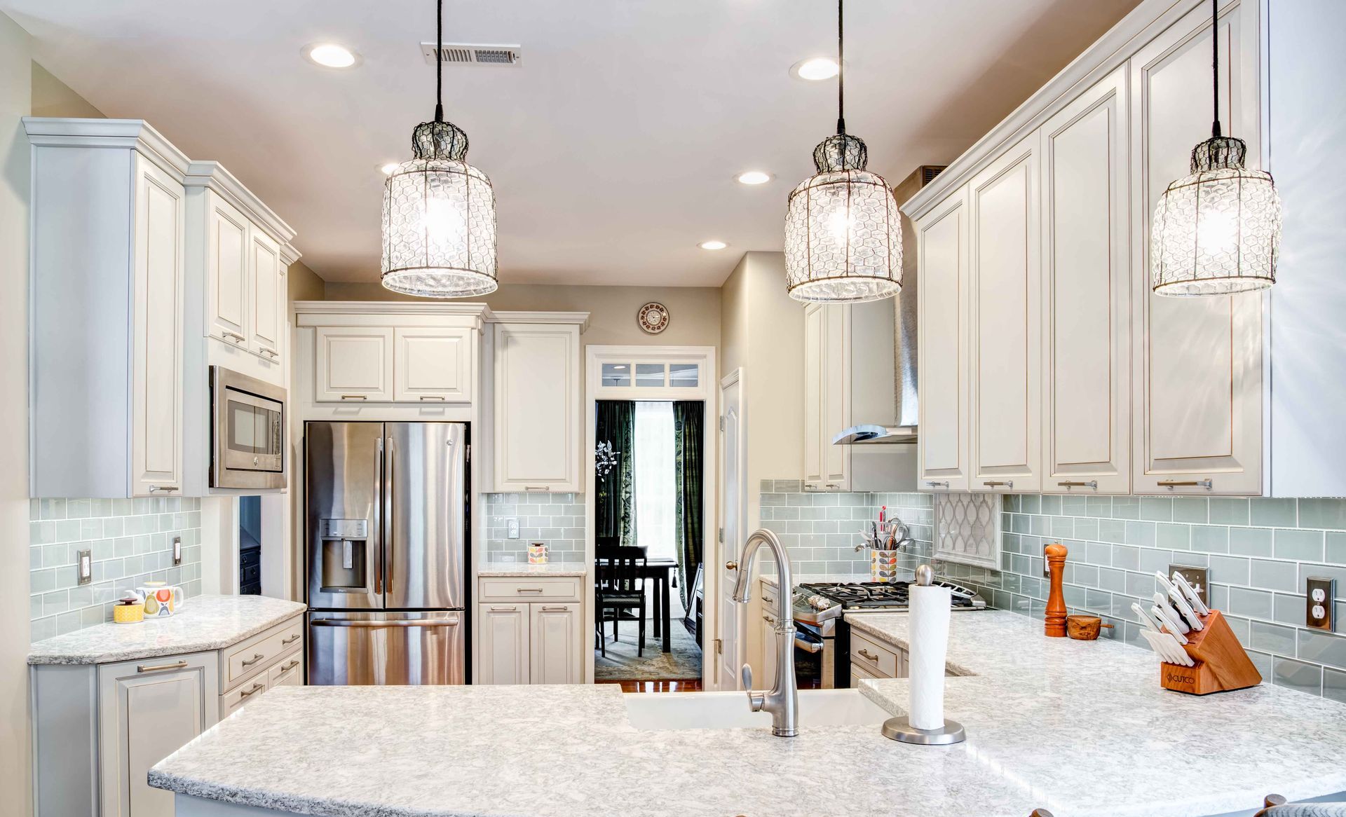 Bright modern kitchen with white cabinets, granite island, stainless fridge, and pendant lights