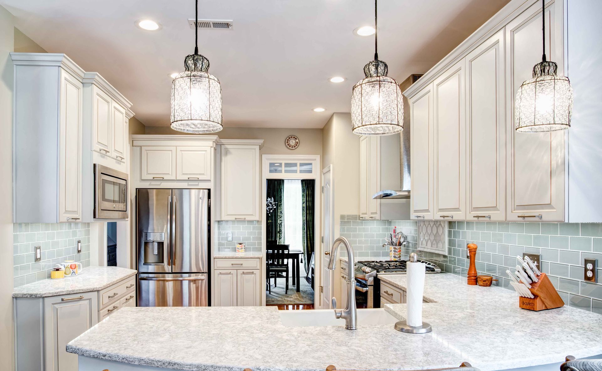 Bright modern kitchen with white cabinets, marble island, stainless fridge, and pendant lights