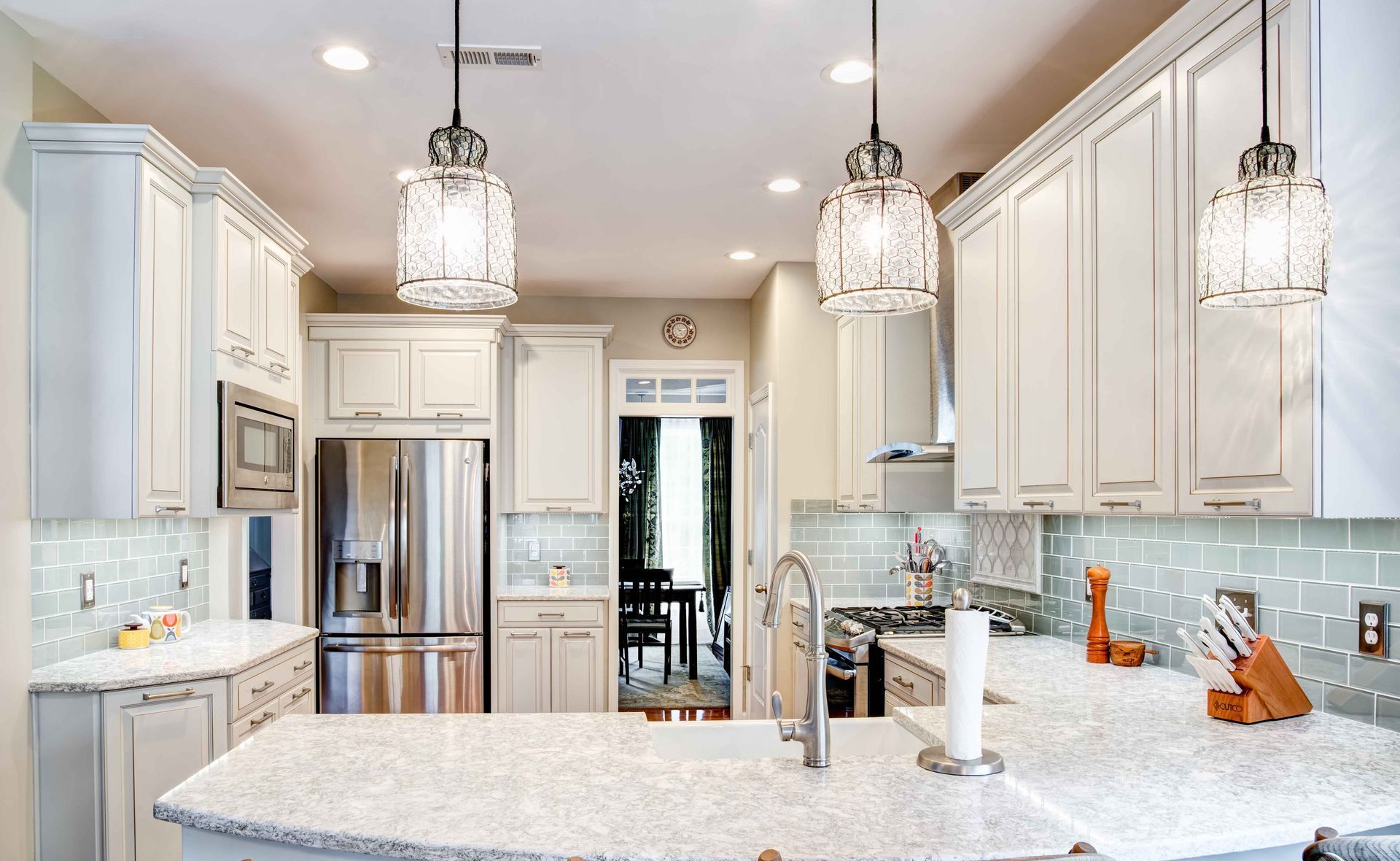 Bright modern kitchen with white cabinets, marble island, stainless steel appliances, and hanging pendant lights