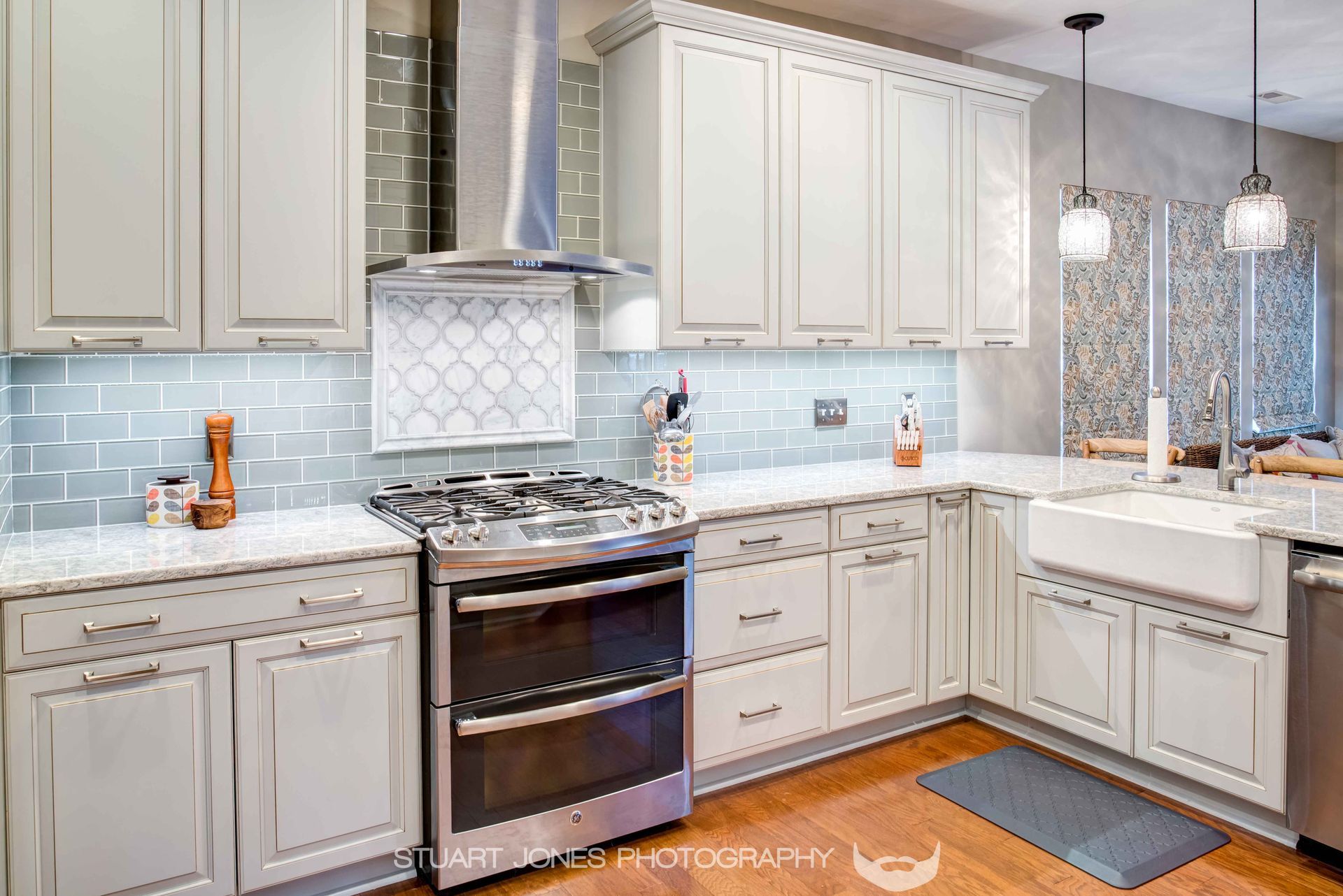 Bright modern kitchen with white cabinets, stainless stove, light blue backsplash, and sunlit breakfast nook.